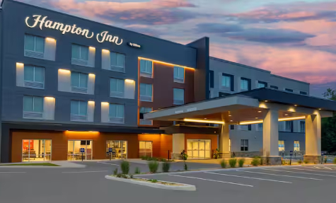 A digital rendering of a large modern hotel with a parking lot in front.