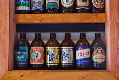 A collection of vintage stubby beer bottles mounted on a wooden shelf.