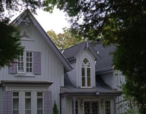 A large gothic purple-gray house with a paved front drive and surrounding trees