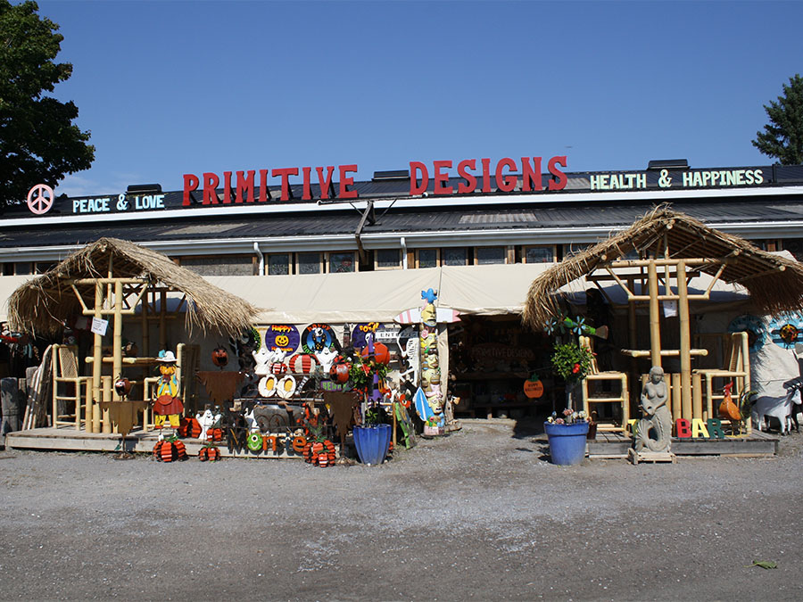 A metal barn with a sign saying "Primitive Designs" and lots of home and garden decor around the entrance.