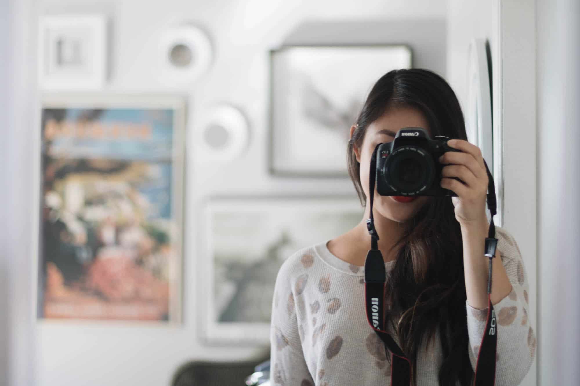 The author, Jessica Lam, taking a photo with her professional camera in the mirror of her bedroom at the Hotel Carlyle. She is in a white top and her face is covered by the camera.