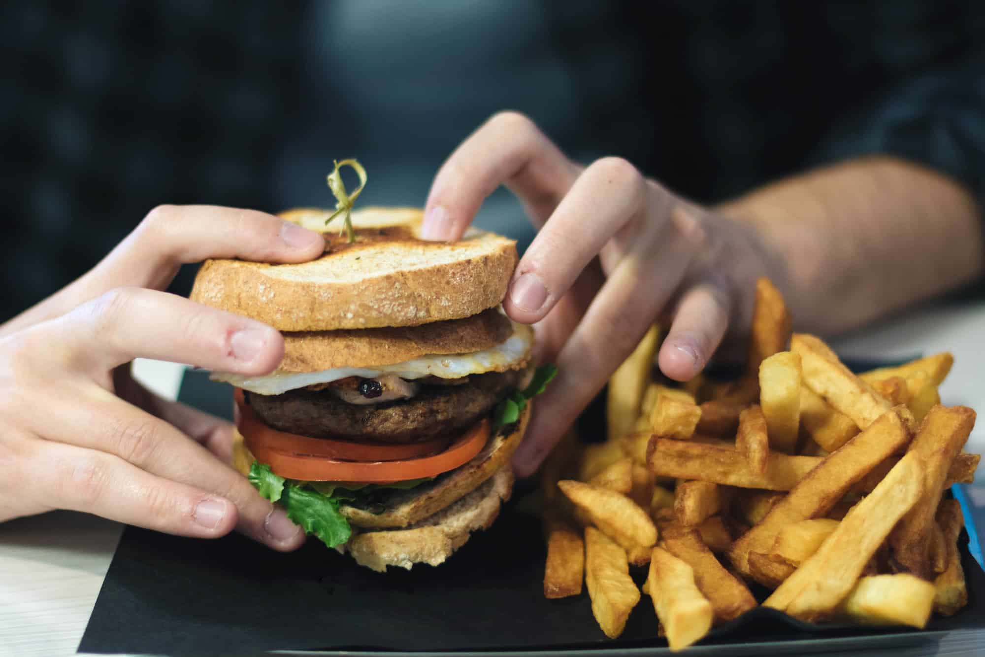 Two hands clutching the Apollo Burger in front of their chest with a side of fries from Olympus Burger in Port Hope