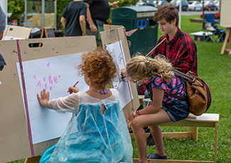 A little girl sitting at an easel and drawing in a park