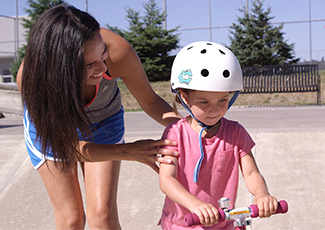 A mother helping her daughter ride a scooter in a stake park