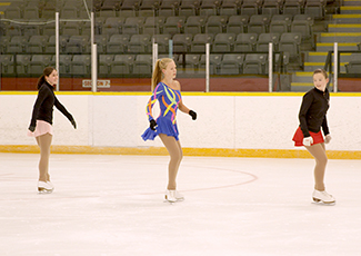 Three young girls skating on an indoor skating rink