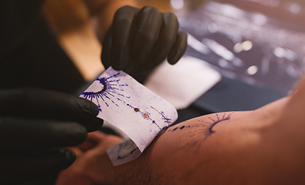 A tattoo artist peeling a sketch transfer off a customer's arm.