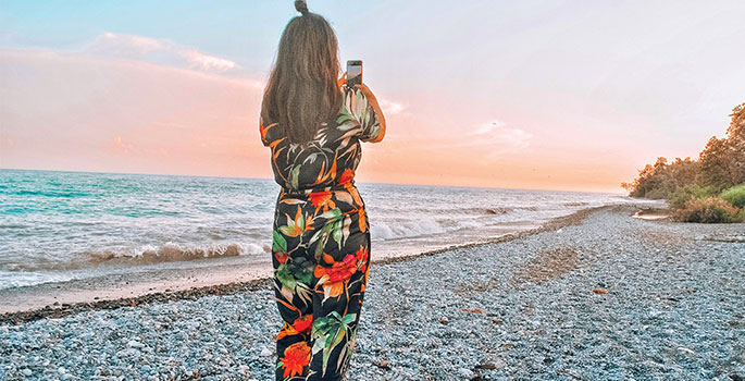 Woman taking a photo of West Beach at sunset in Port Hope